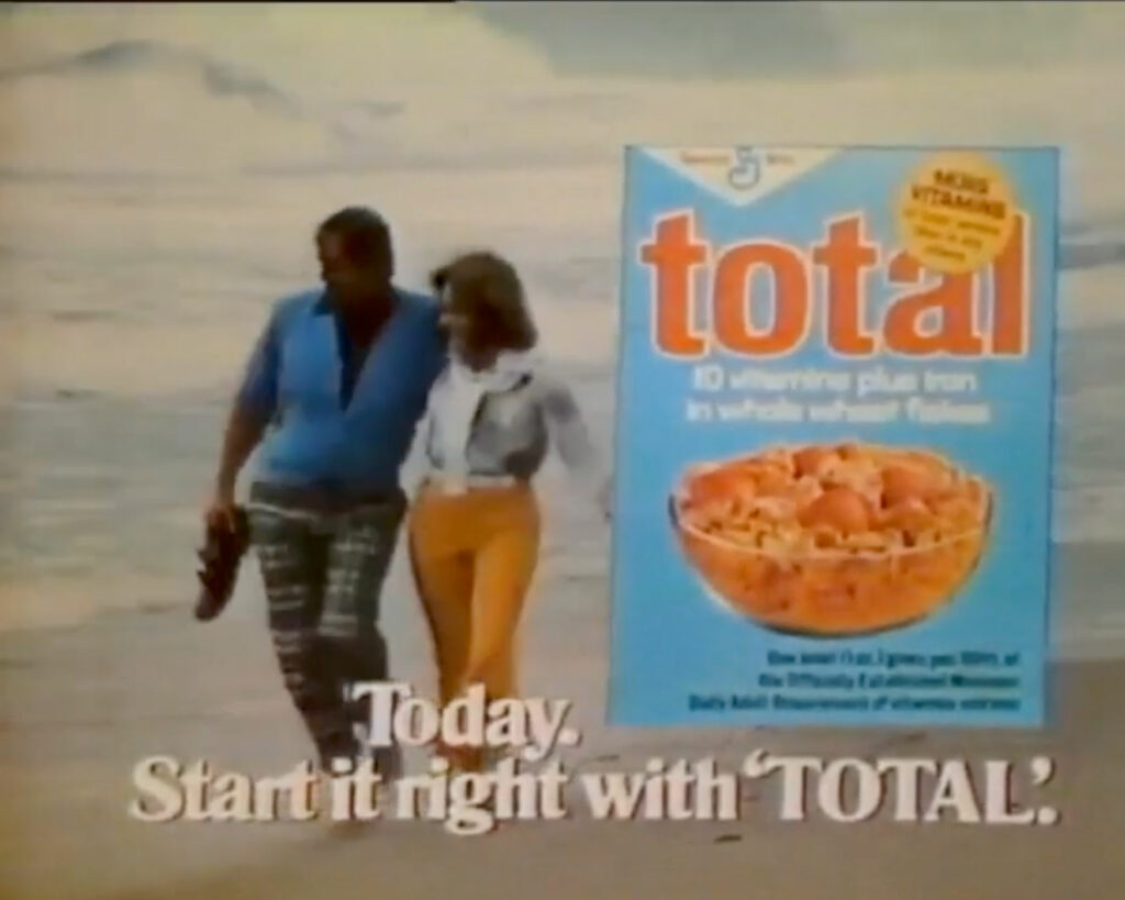 A vintage advertisement for Total cereal; a couple, a man in a blue top with plaid pants and a woman wearing a white blouse and yellow slacks, walk along a beach arm in arm. Overlaid on top is an image of a blue box of Total-brand cereal. On-screen text reads, "Today. Start it right with 'TOTAL'."