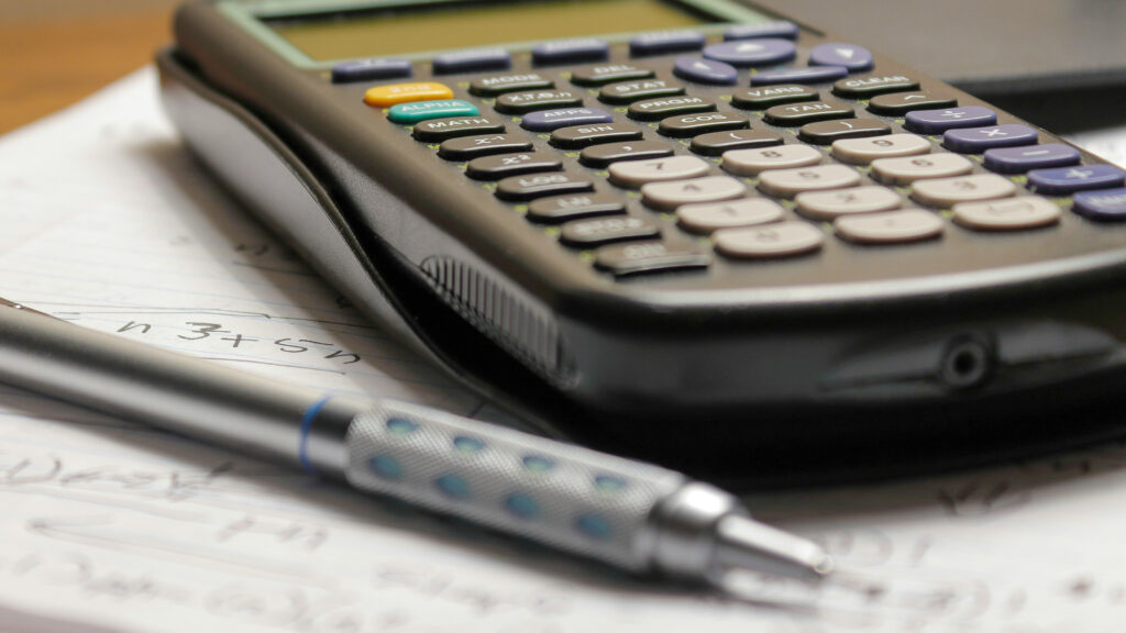 A close up photo of a graphing calculator and metal mechanical pencil working out an equation on lined paper.